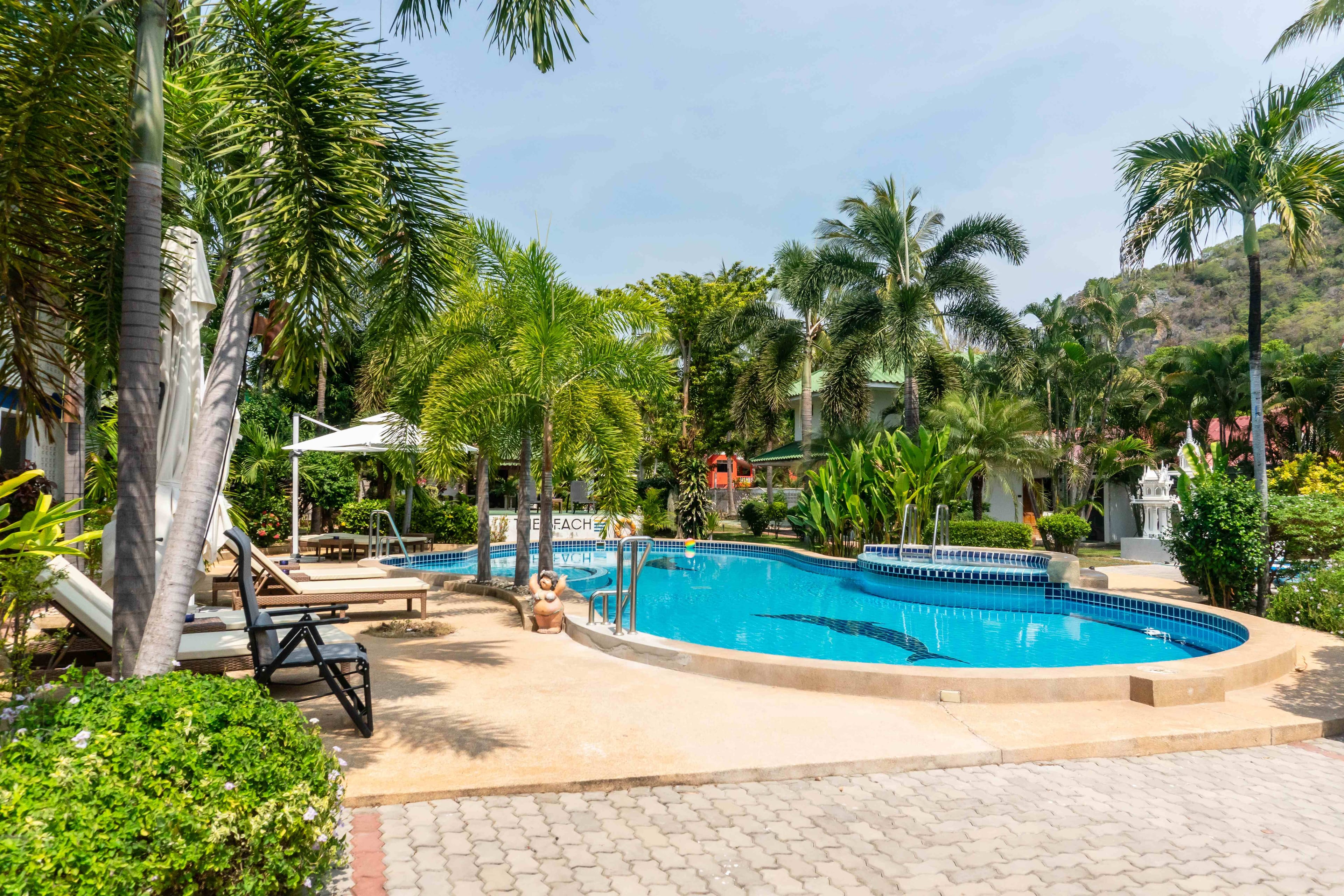 Poolanlage von The Beach Altersresidenz Thailand mit Palmen, Liegestühlen und Bergpanorama im Hintergrund