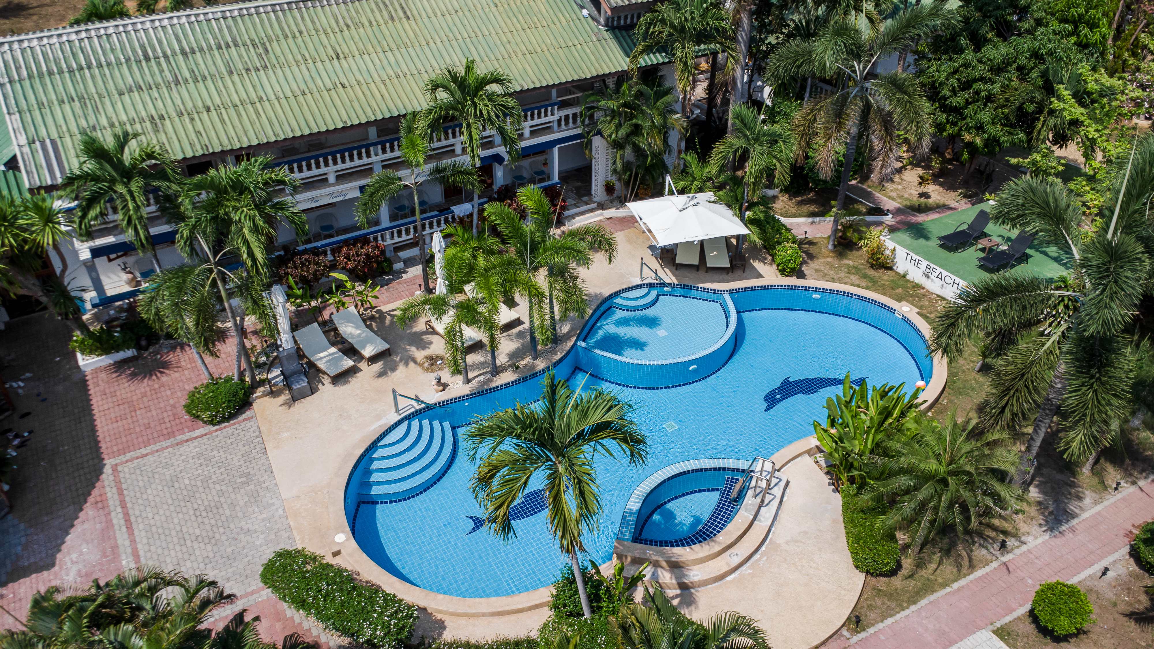Luftaufnahme der Poolanlage von The Beach Altersresidenz Thailand mit delfinförmigem Pool, Palmen und Loungern